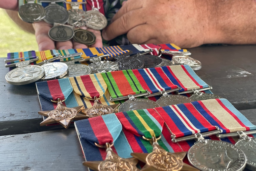 Rows of war medals lined up on table and some being held by a man.