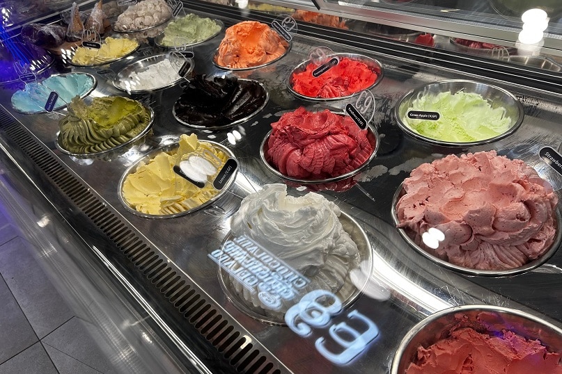 Pink, orange, yellow, green, red, and blue-coloured ice cream in a cabinet in a shop.