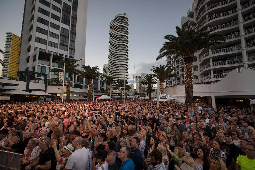 Crowd fills Broadbeach street for a live blues set among high-rise buildings at sunset.