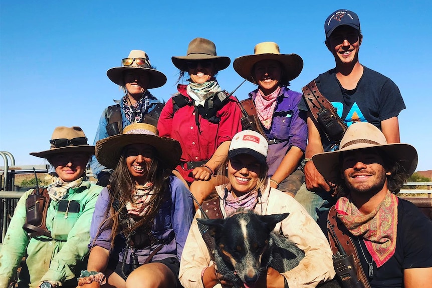 A group of six young female ringers and two male ringers wearing hats posing for group photo with dog