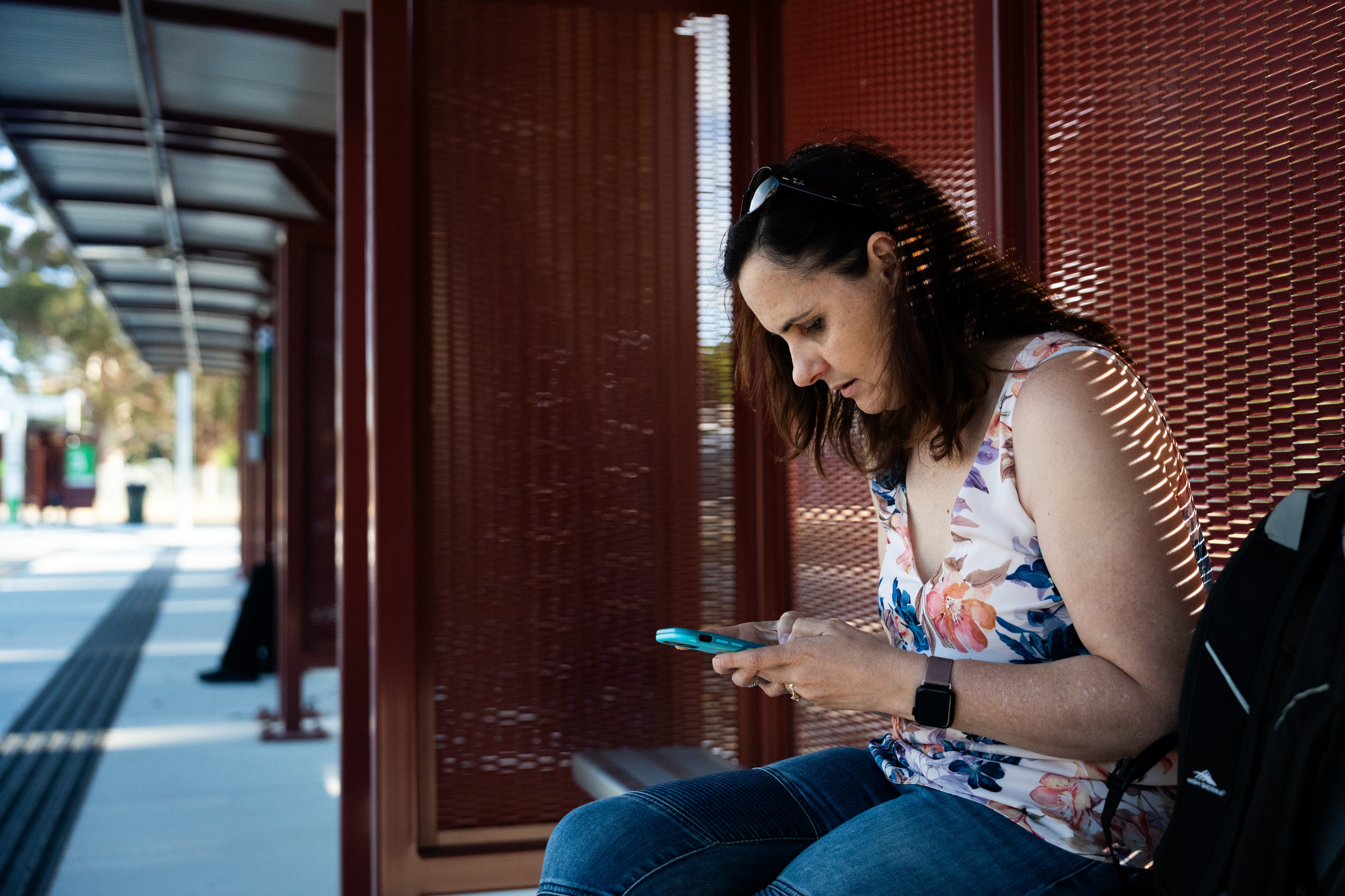 A woman sitting on a bench at a bus station, using her phone.