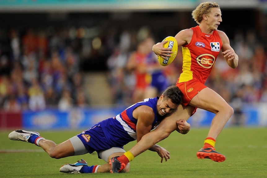 Gold Coast's Trent McKenzie is tackled by the Western Bulldogs' Daniel Giansiracusa.