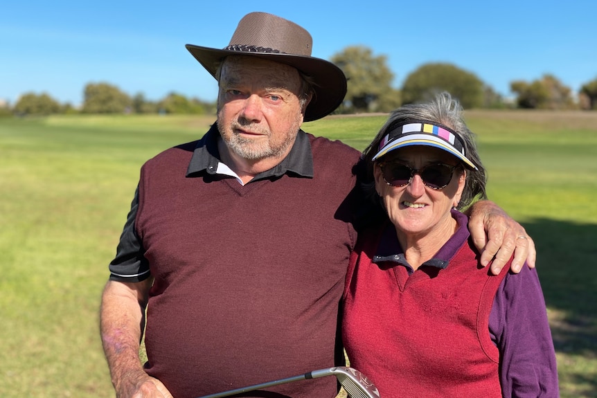 A man and a woman on a golf course wrap their arms around each other's shoulders.