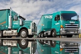 Two trucks from transport company Toll reflected in a pool of water.