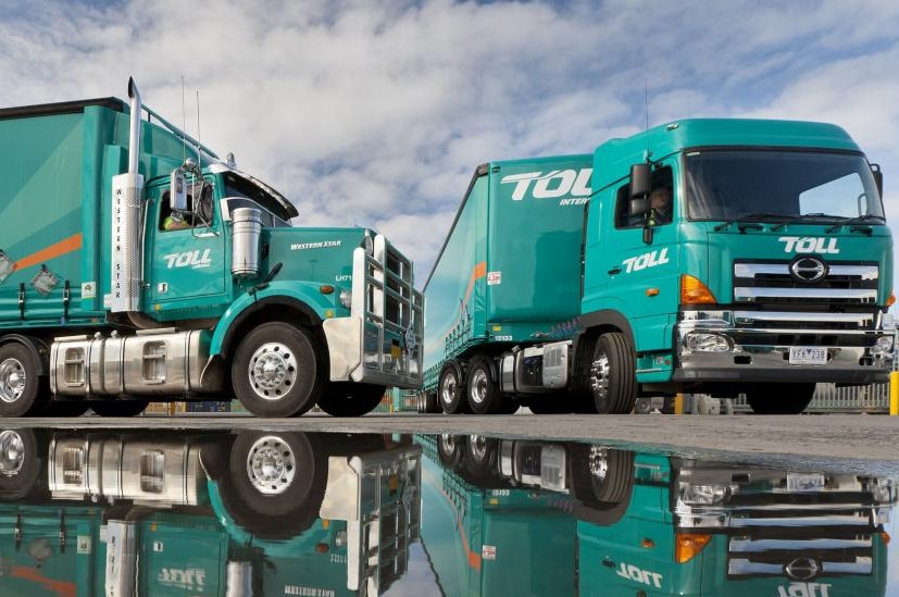 Two trucks from transport company Toll reflected in a pool of water.