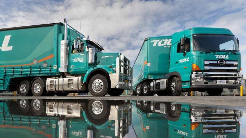 Two trucks of the transport company Toll are reflected in a pool of water.