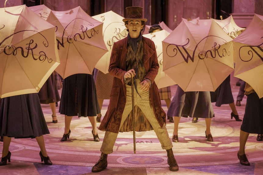 Timothée Chalamet performs a musical number on set as Wonka, surrounded by women twirling 'Wonka' umbrellas in front of them.