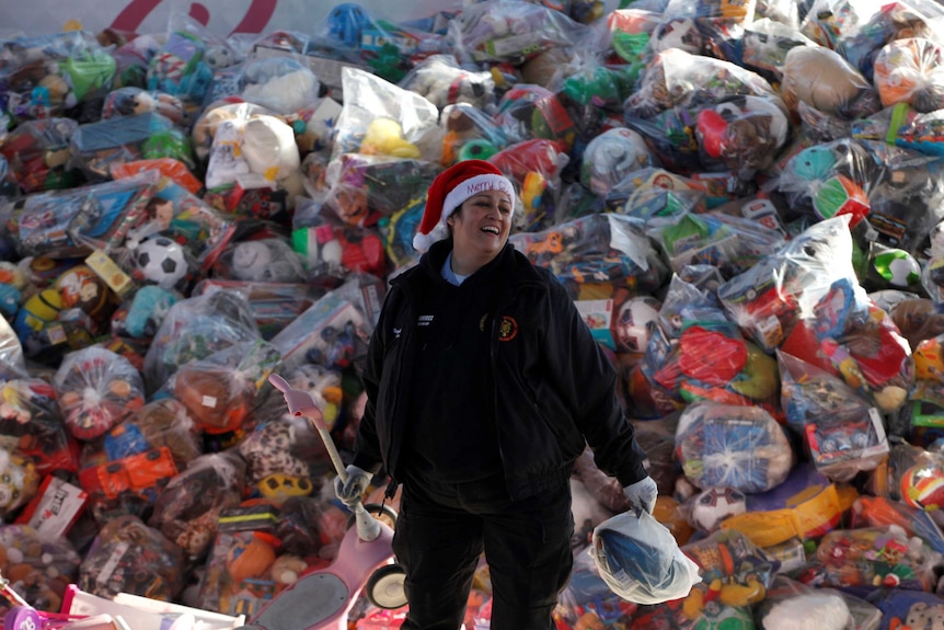 A volunteer smiles as she stands next to bags with toys