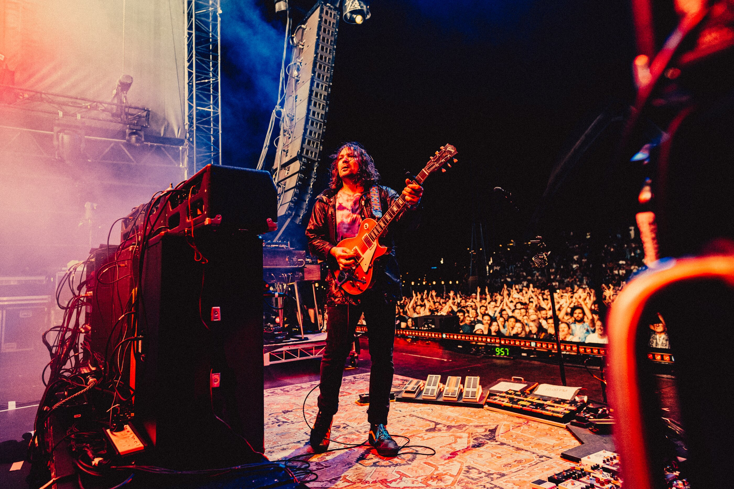 Adam Granduciel holding a guitar, facing a speaker stack with his back to a large crowd
