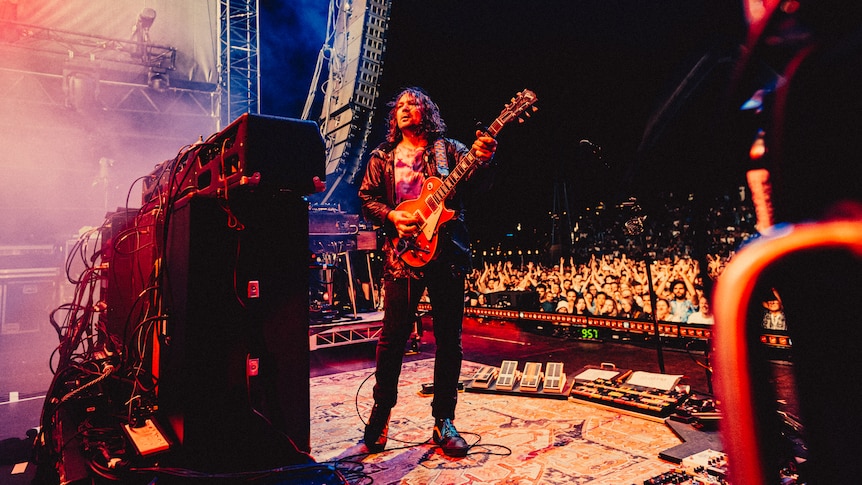Adam Granduciel holding a guitar, facing a speaker stack with his back to a large crowd