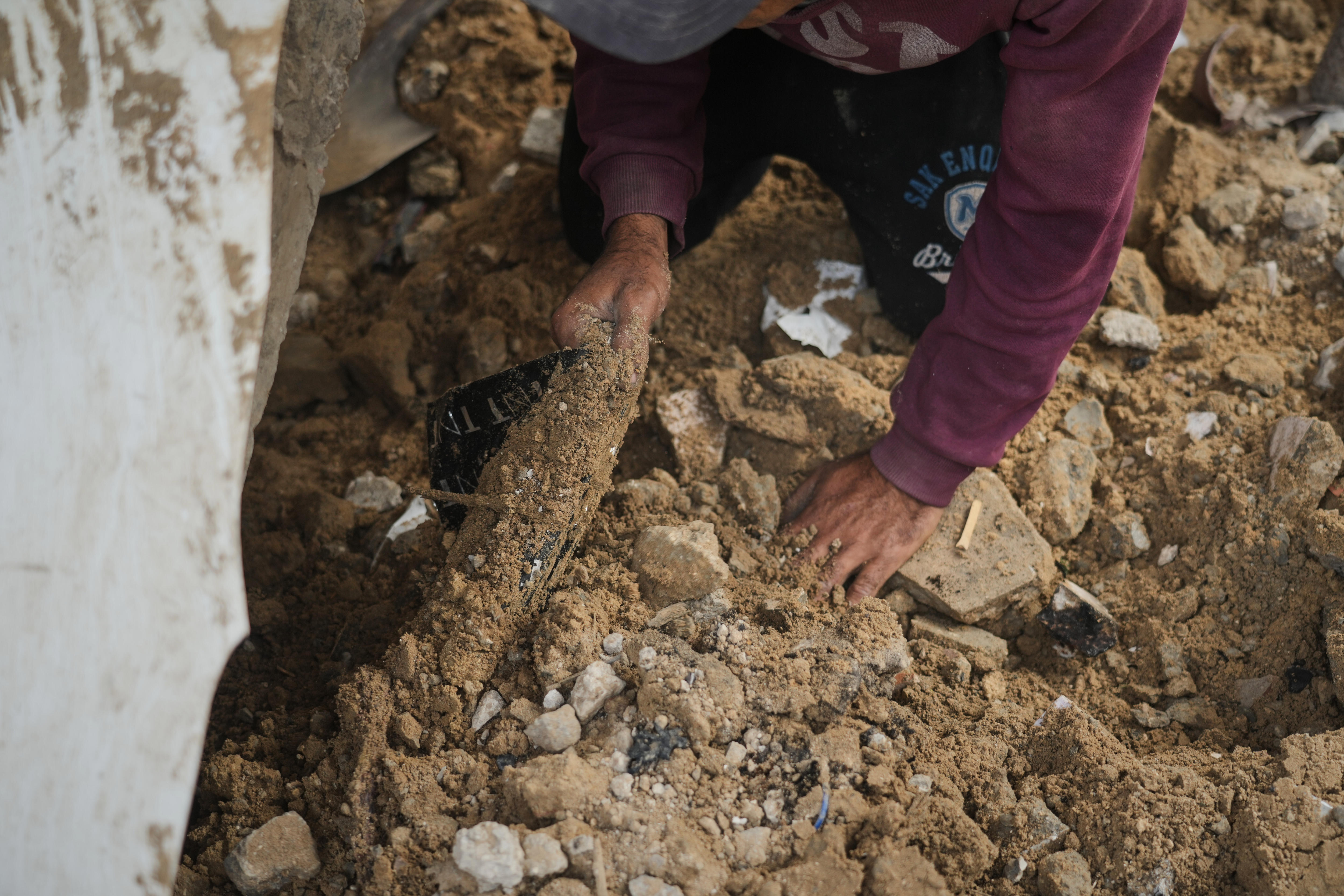 Um par de mãos procurando ossos entre a sujeira e os estilhaços.