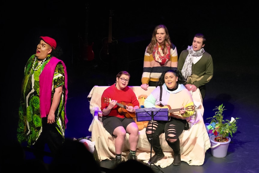 Five actors are performing a song on stage with ukuleles