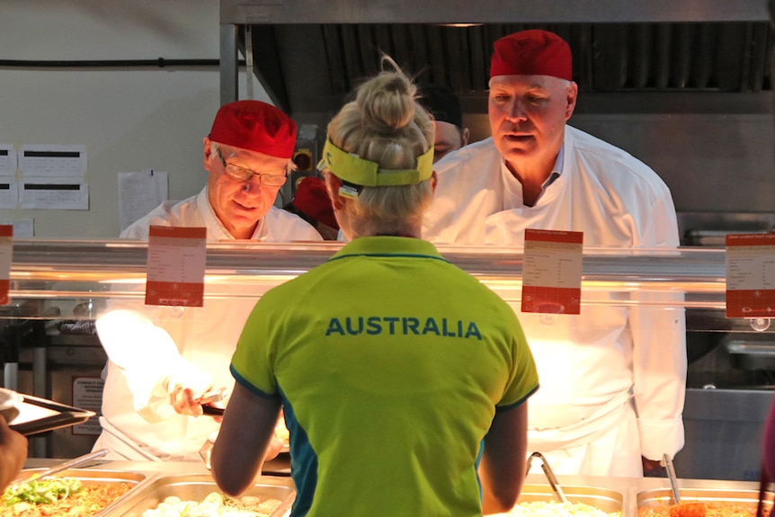 GOLDOC chair Peter Beattie and CEO Mark Peters serve food at the Athletes Village