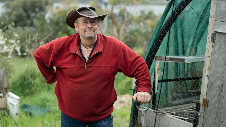 Malcolm Battersby stands next to a garden greenhouse.