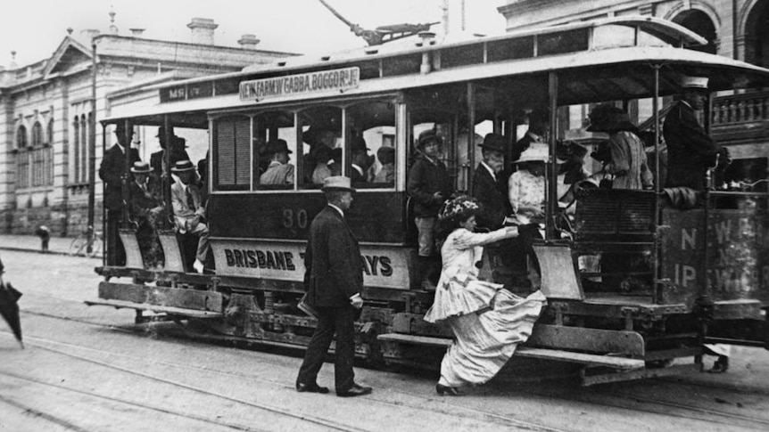 Woman wearing a long dress, hat and shoes, getting onto a Brisbane tram