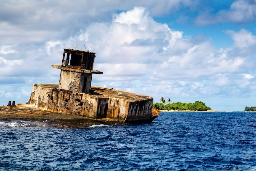 A rusty shipwreck in Enetewak Atoll with an island behind.