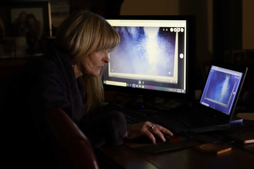 A woman in a dimly lit room looks at CCTV on a two computer screens