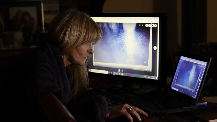 A woman in a dimly lit room looks at CCTV on a two computer screens
