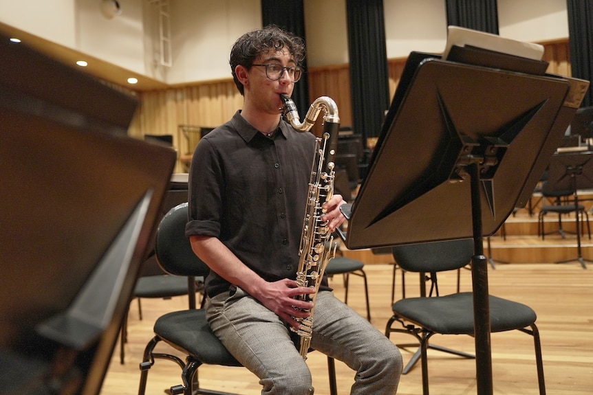 Hugo sits on a stage playing the clarinet