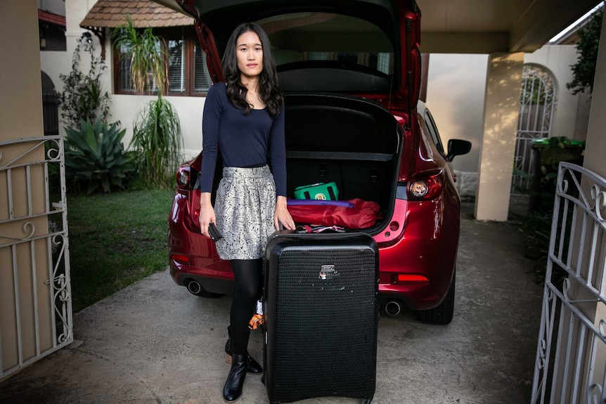 a woman standing behind a car with the boot open, next to a luggage bag