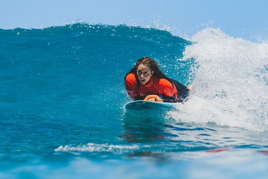 A woman surfing with a blue sky visible in the background