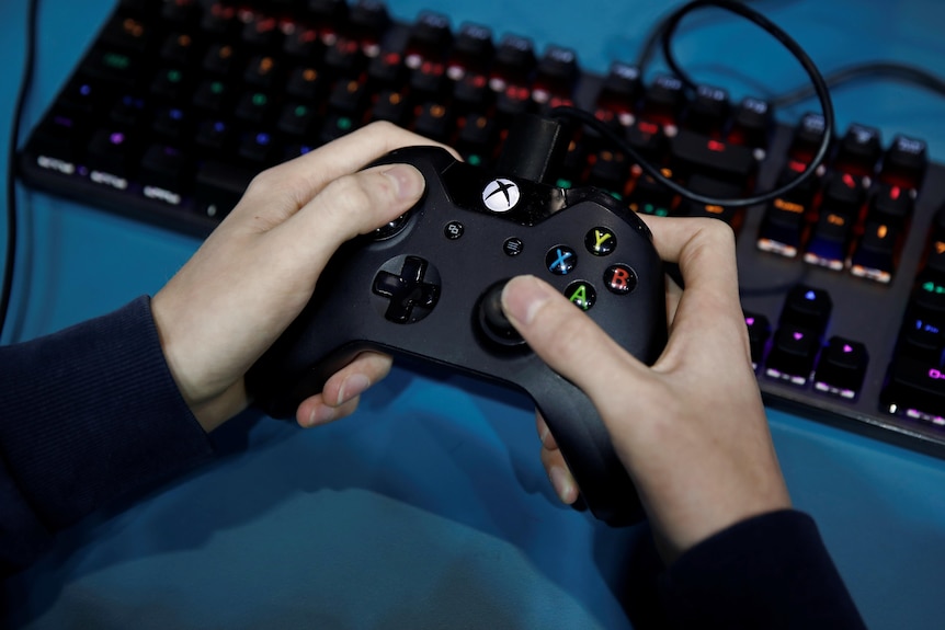 Two hands hold an xbox controller above a black keyboard