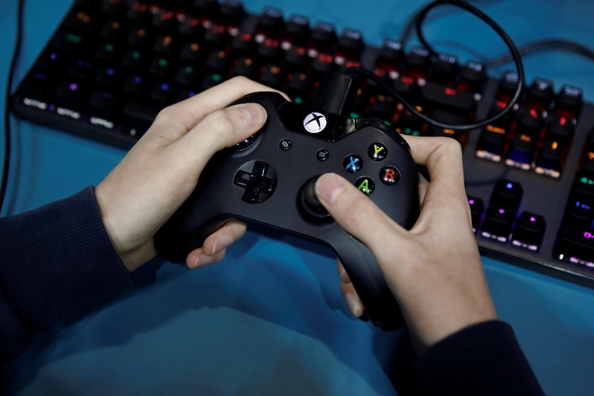 Dos manos sostienen un controlador de Xbox sobre un teclado negro