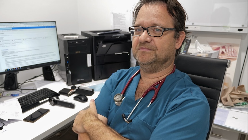 A doctor in dark blue scrubs and glasses, wearing a stethoscope around his neck.