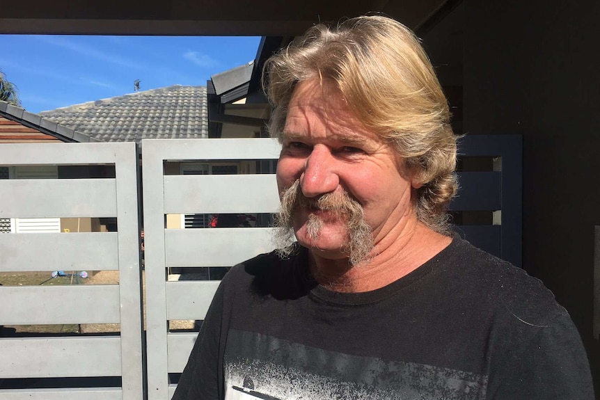 Ross Hedge smiles as he stands outside the gate to his home