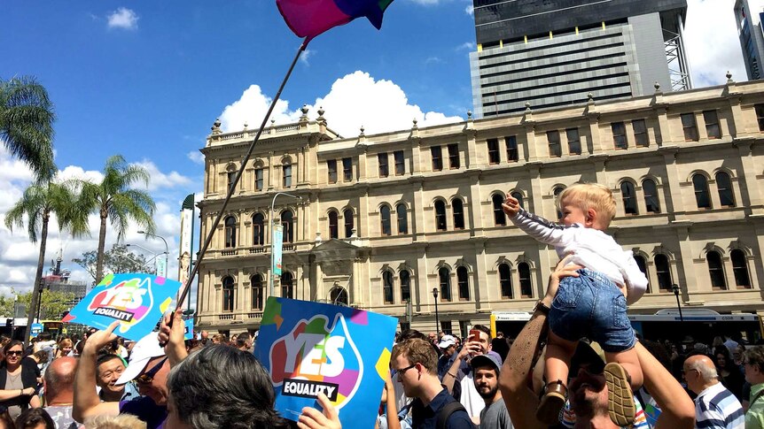 A rainbow flag is hoisted among a crowd in the Brisbane CBD