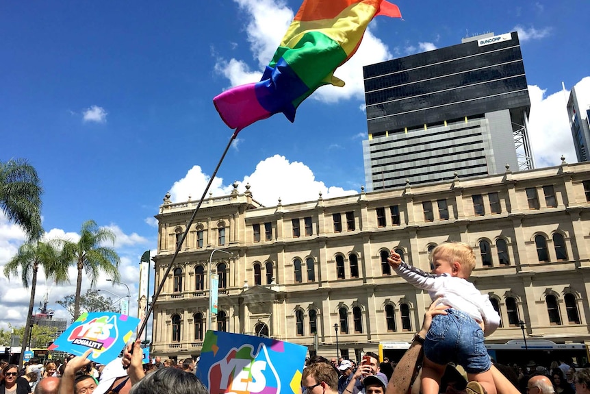 A rainbow flag is hoisted among a crowd in the Brisbane CBD