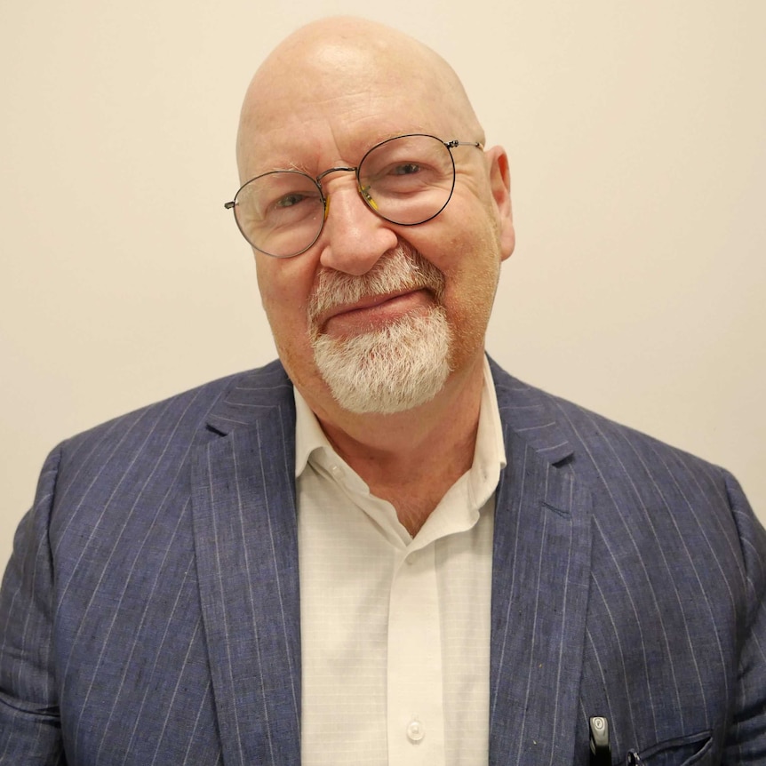 A middle aged man with glasses and a white goatee smirks at the camera