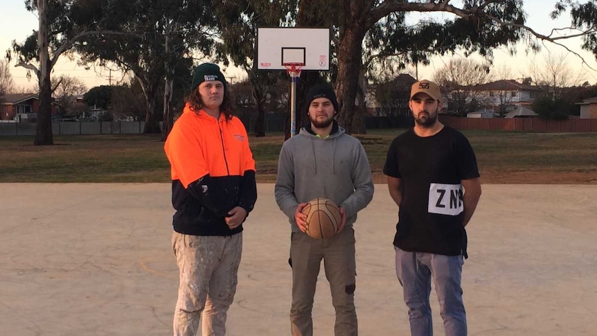 Three young men standing on a basketball court which was named after their friend Joseph Mateo who took his own life.