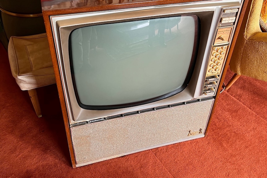 An old television sits on red carpet.