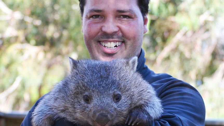 A smiling man holds a wombat in his arms