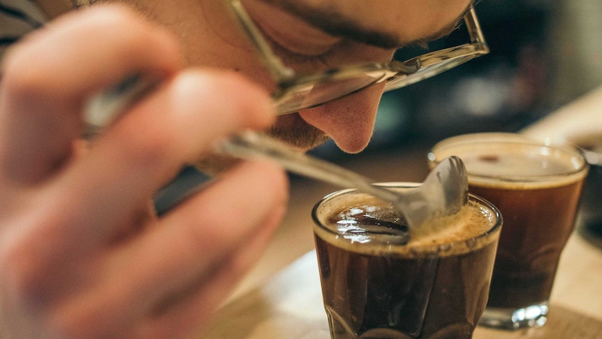 A person leans forward to sniff a glass of black coffee.