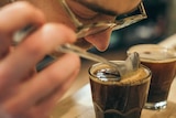 A person leans forward to sniff a glass of black coffee.