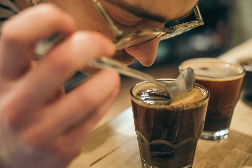 A person leans forward to sniff a glass of black coffee.