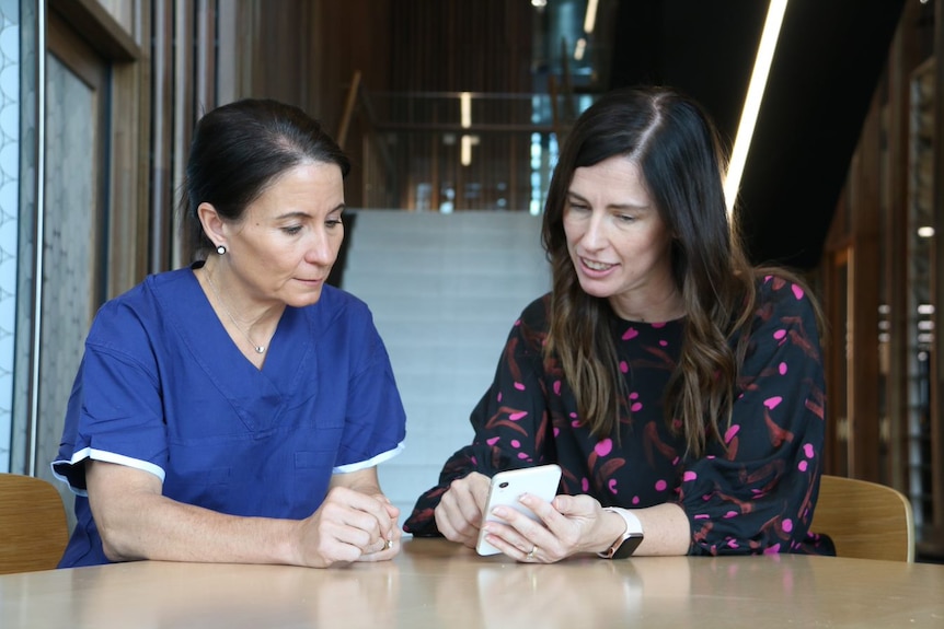 Two women look at a phone while sitting at a table
