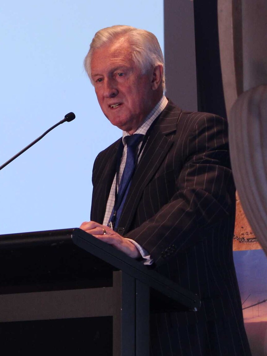 An older man, suited, stands grimacing at a lecture. This is former Liberal leader John Hewson.