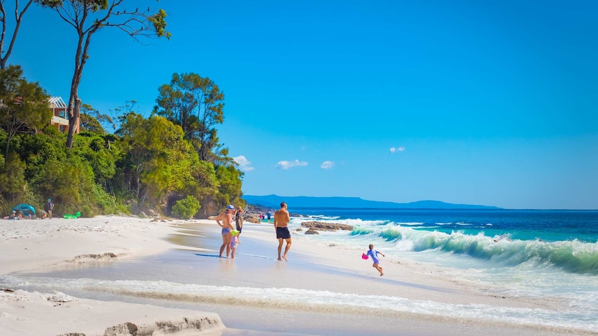 A group of people look out to the ocean as a wave is about to crash near the.