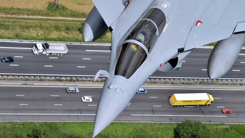 A French Rafale jet flies over a highway.