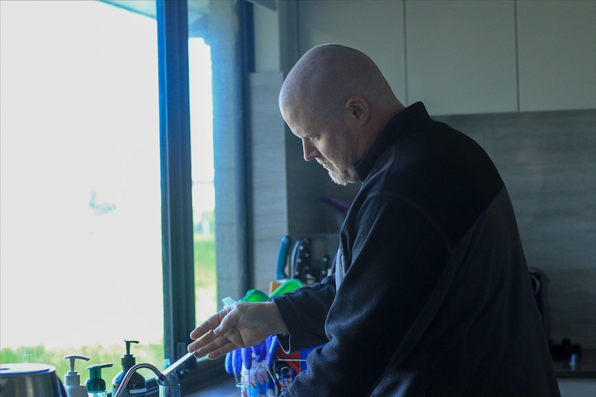 A picture of Mark Pember at the sink in front of a window inside a house