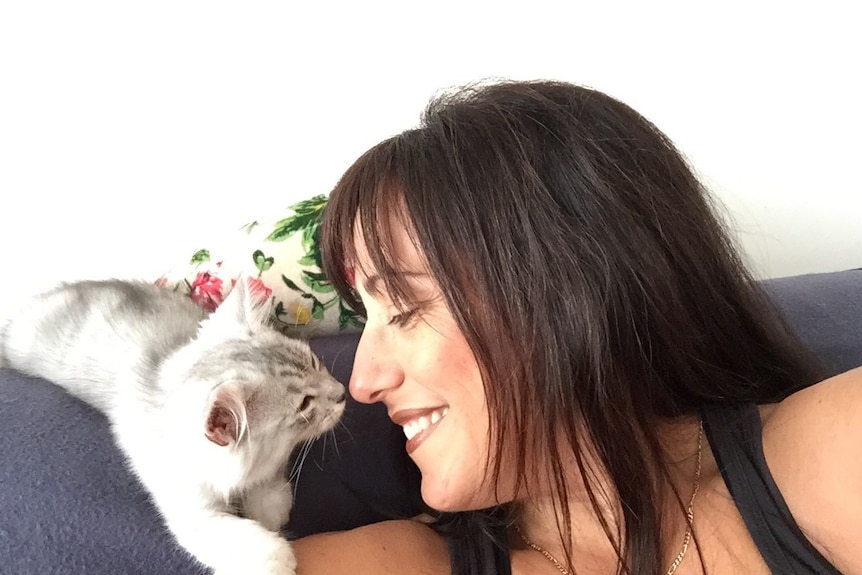 Carmen smiles with a kitten on the couch.