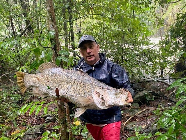man in rain jacket holding large barramundi