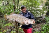 man in rain jacket holding large barramundi