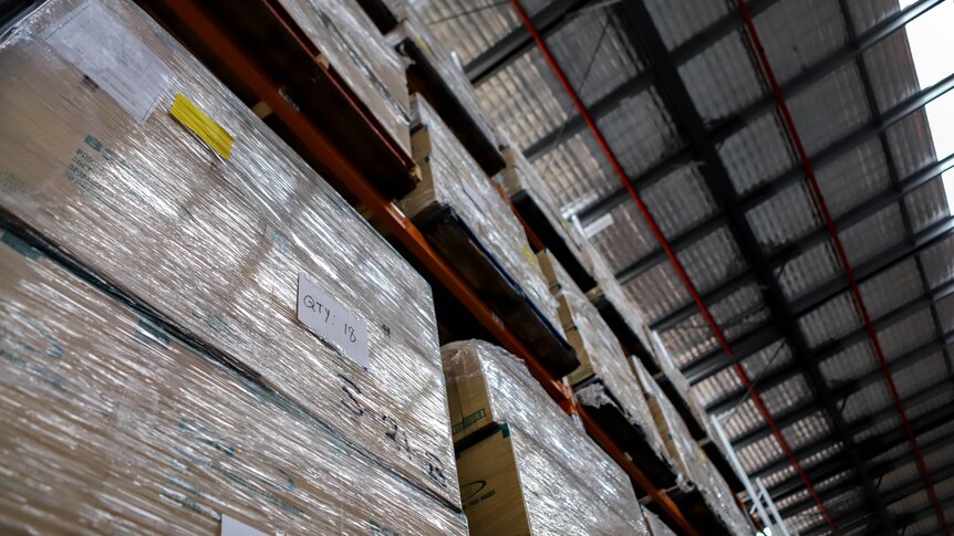 Large concrete floor warehouse with rows of boxes of medical equipment stacked high beneath a silver padded roof