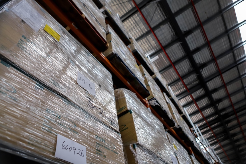 Large concrete floor warehouse with rows of boxes of medical equipment stacked high beneath a silver padded roof