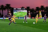 A-League game plays with a big screen, the sunset and some giant sauce bottles in the background.
