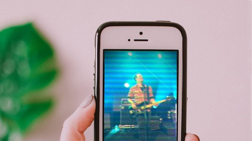 A hand holds a phone showing a musician playing bass guitar